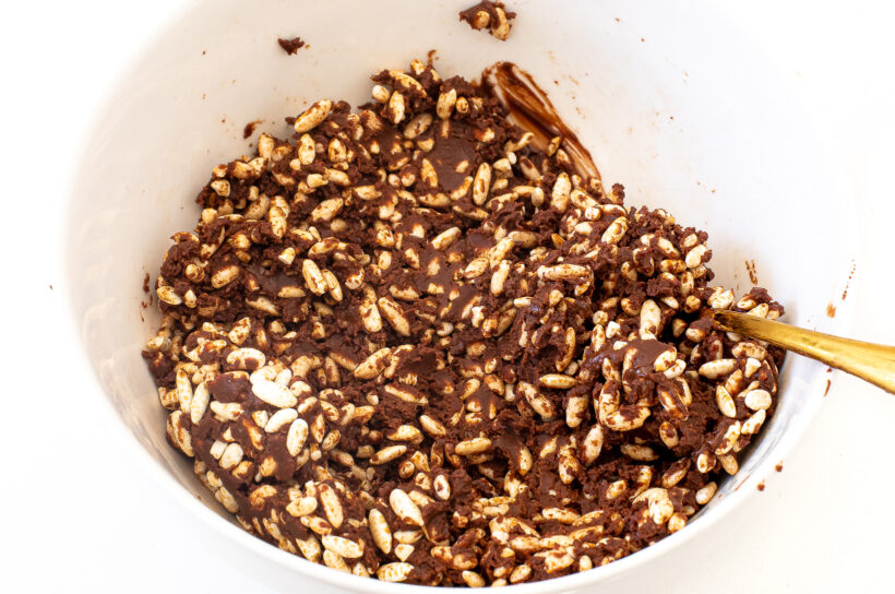 Chocolate mixture added to crispy rice in a white bowl.