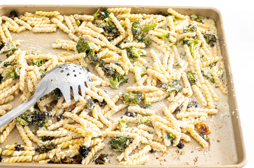 Pasta, boursin cheese, and broccoli being mixed together on a sheet pan. 