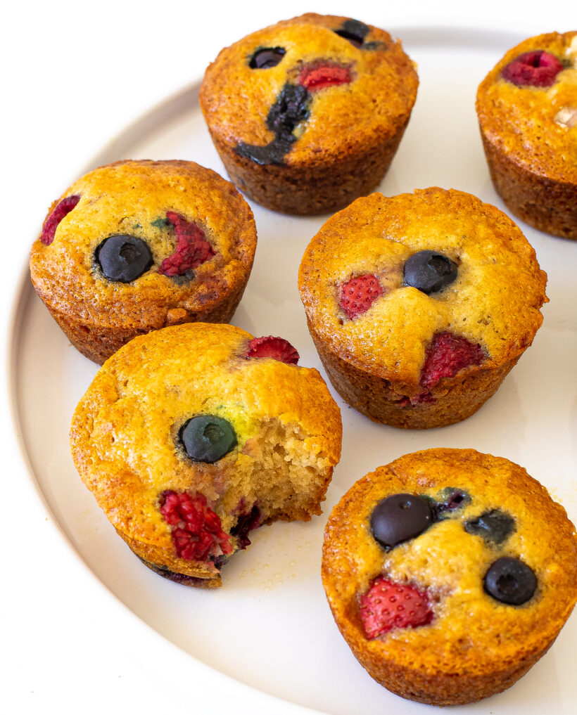 Berry yogurt muffins on a plate with one muffin missing a bite.