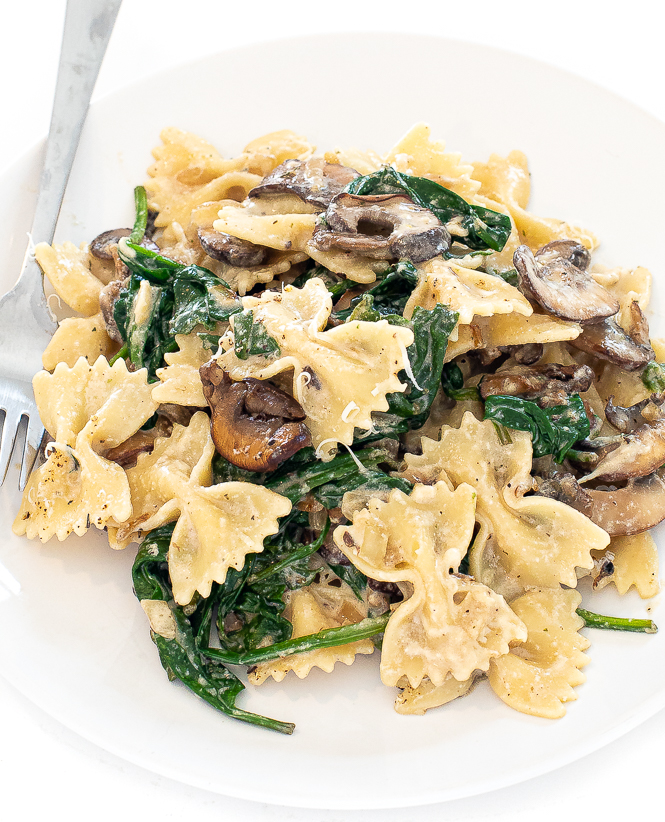 Mushroom spinach pasta in a white bowl with a silver fork.