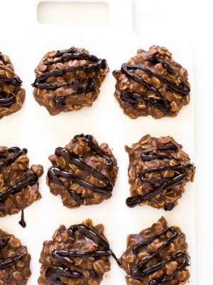 Chocolate oatmeal cookies with chocolate drizzle laid in rows on white cutting board.