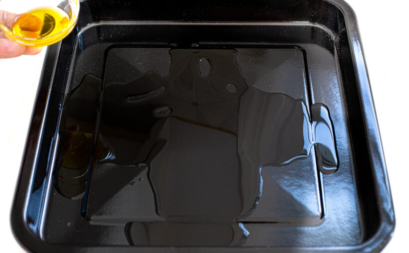 Hand pouring olive oil into pizza pan.