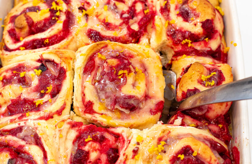 Orange cranberry rolls after being baked with a spatula picking one up.