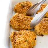crispy oven fried chicken in a white baking dish with metal tongs