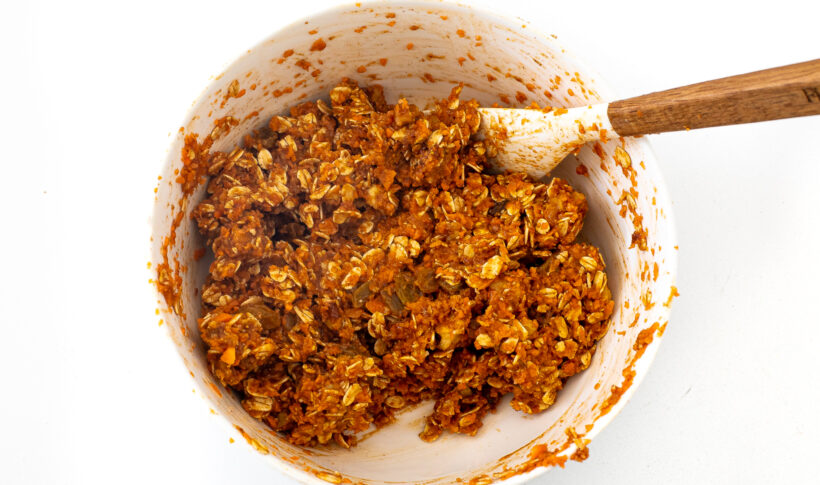 Energy balls mixture mixed in a large white bowl with a rubber spatula.