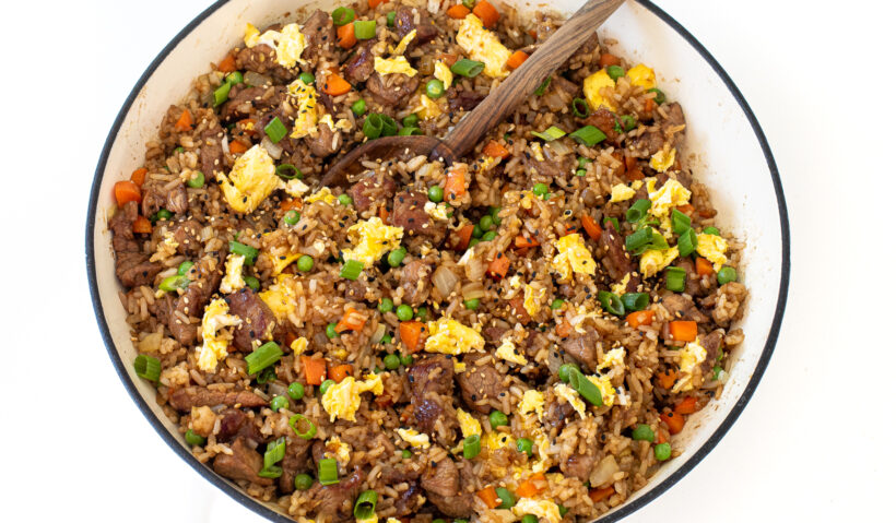 Pork fried rice after being cooked in a skillet with a wooden spoon.