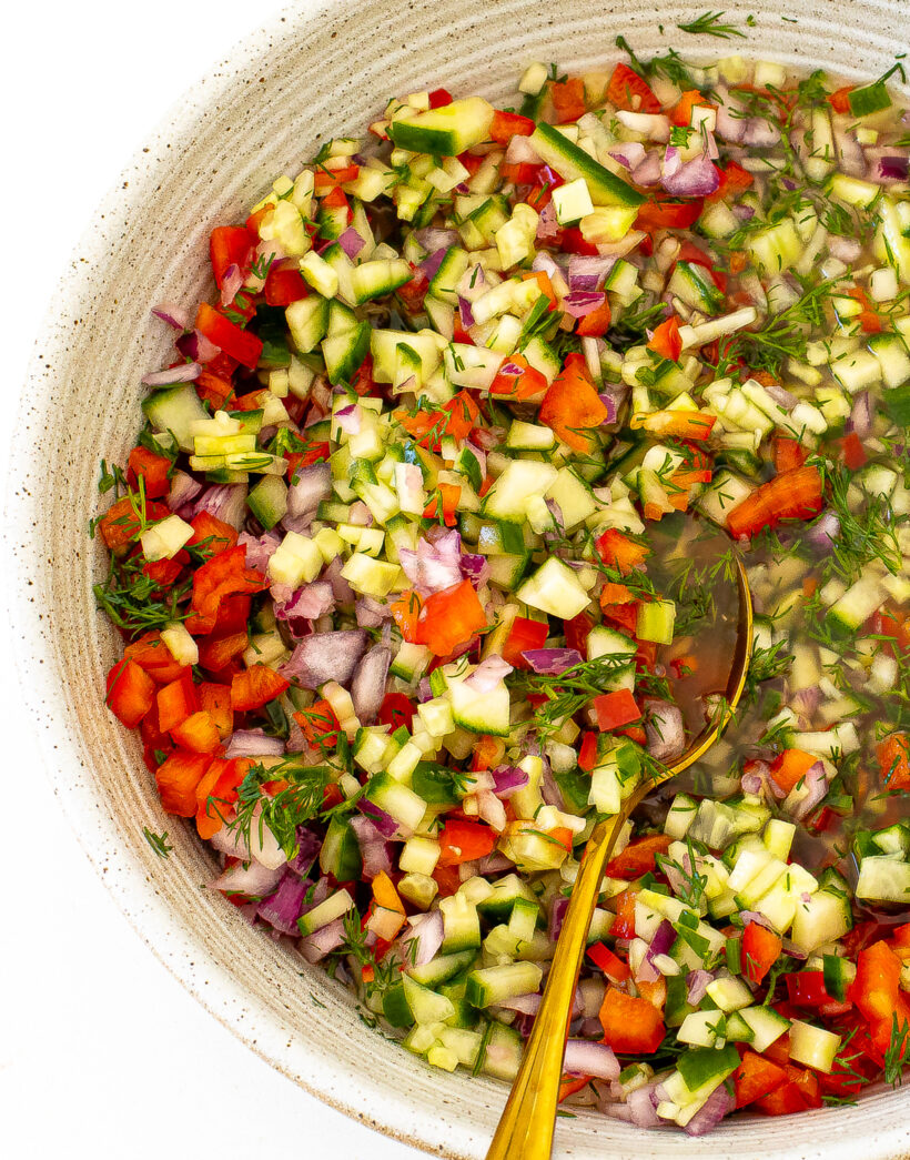 A bowl of pickle de gallo with a gold spoon in it.