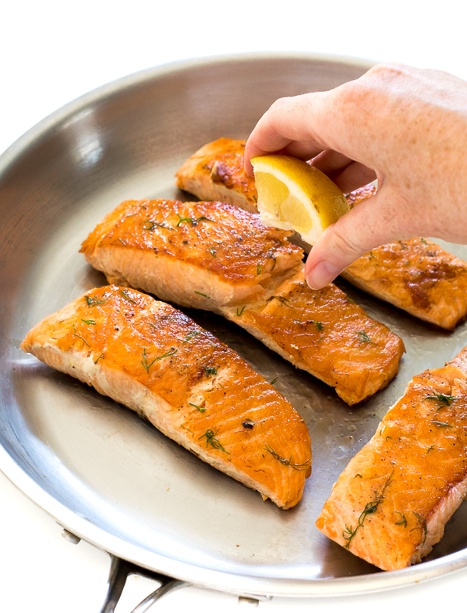 Easy Salmon with Lemon Dill Butter | chefsavvy.com A hand squeezing lemon onto salmon with dill.