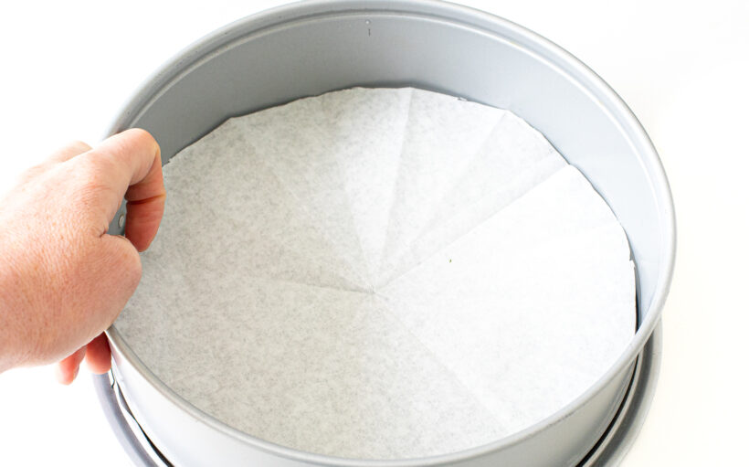 Hand lining springform pan with parchment paper.