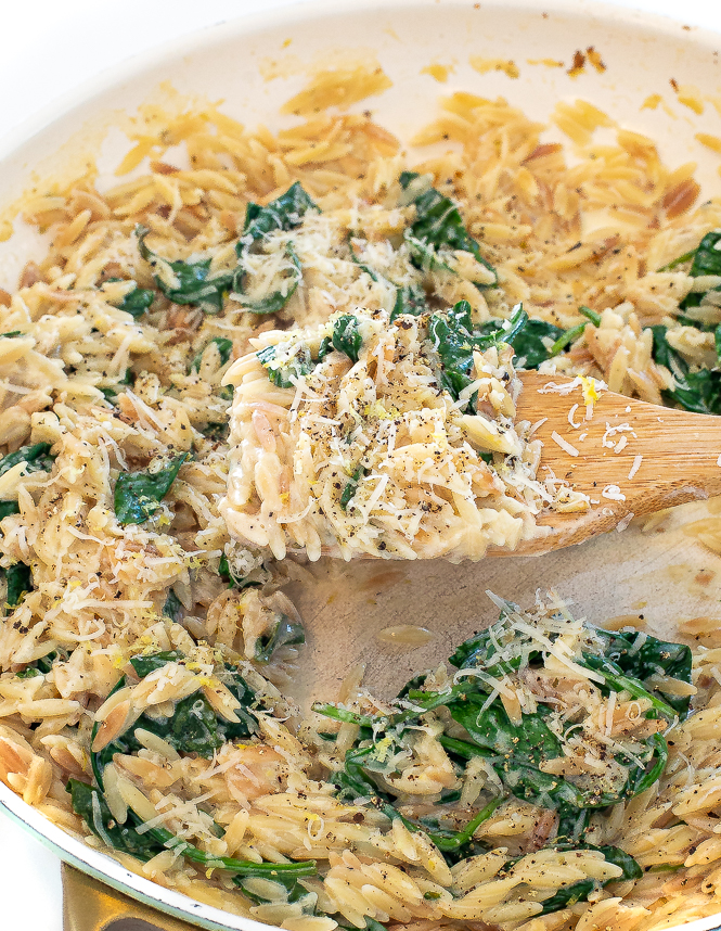 Wooden spoon scooping up orzo out of a skillet.