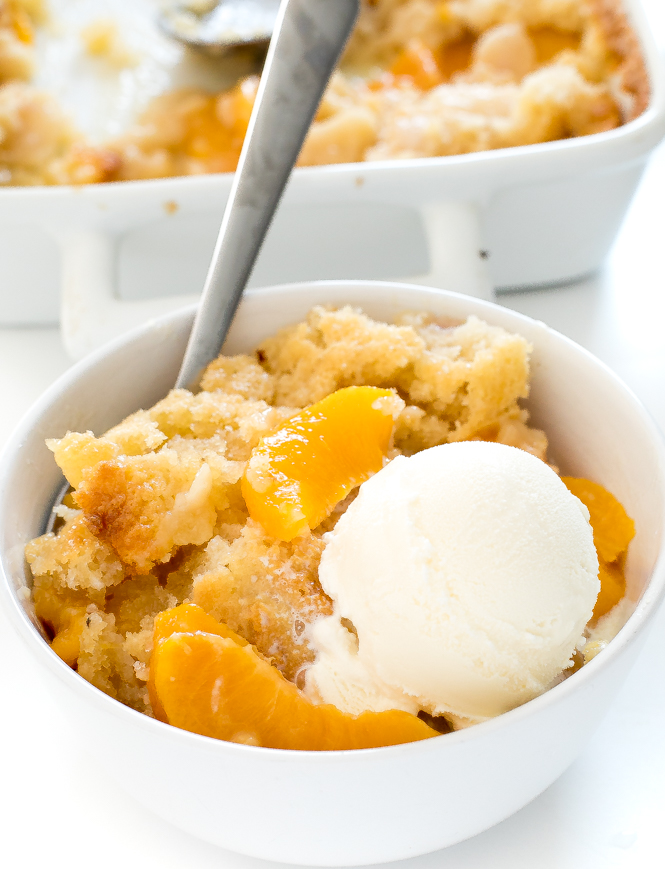 peach cobbler in white bowl with vanilla ice cream on top