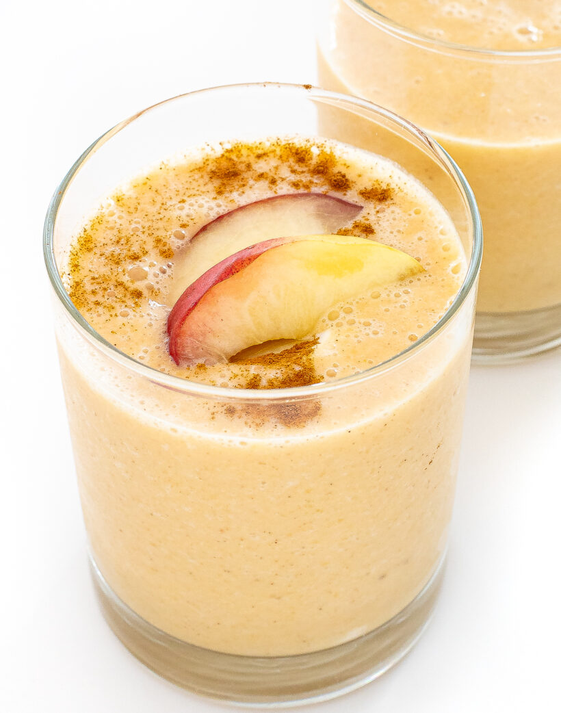 Peach smoothie in a glass with peach slices and cinnamon on top.