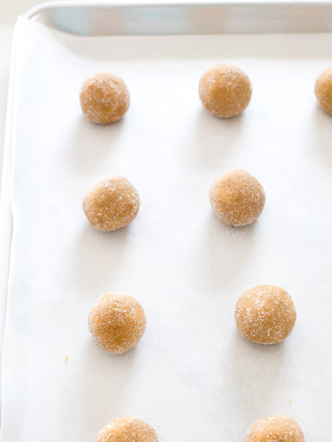 peanut butter cookie dough rolled in small balls and coated with sugar, set on a baking sheet