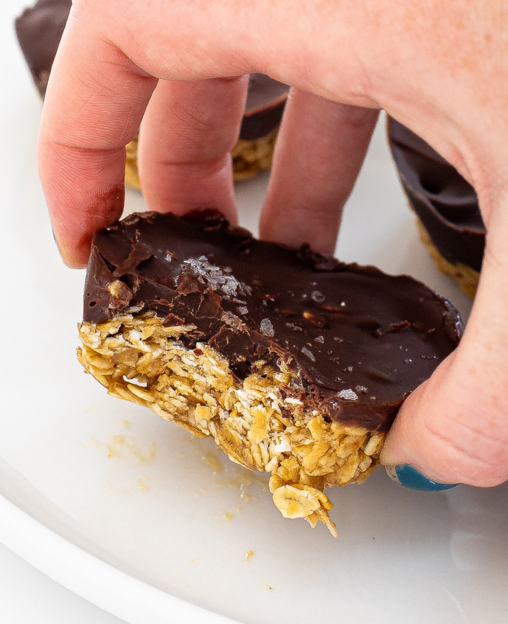 Hand holding a peanut butter oat cup that has a bite taken out of it. 