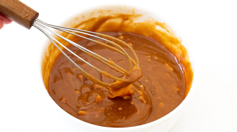 Peanut salad dressing in a small bowl with a whisk. 