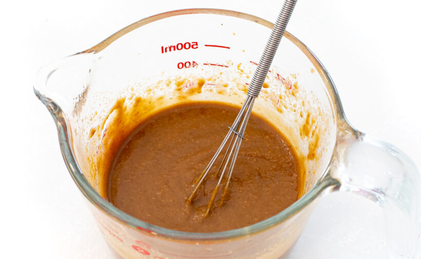 Peanut sauce in a measuring cup with a small whisk. 