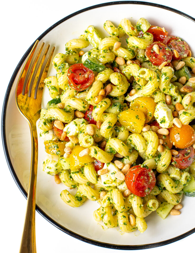 Pesto pasta salad on a white plate with a gold fork.