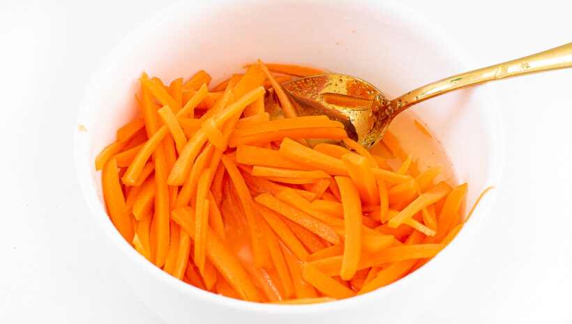 Shredded carrots being pickled in a small white bowl.