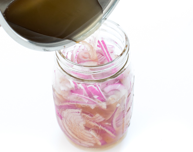Pouring vinegar into mason jar with sliced red onions.