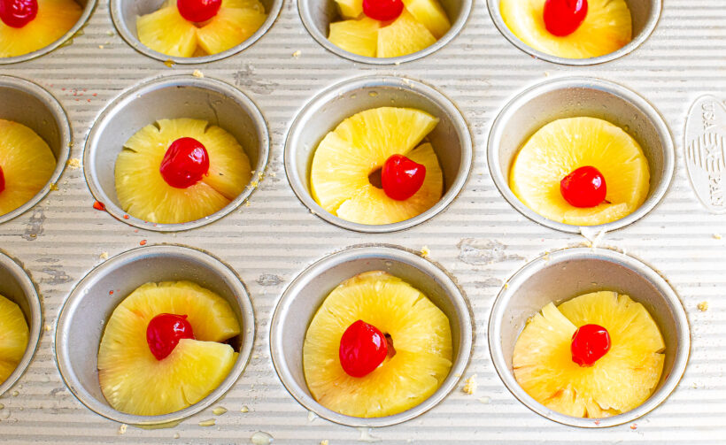 Pineapple rings and cherries in a muffin tin.