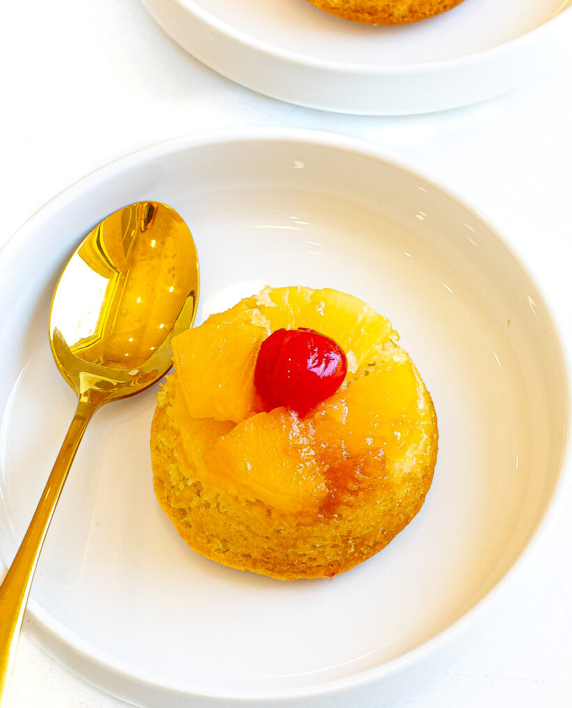 Upside down pineapple mini cake served on a plate with a golden spoon.
