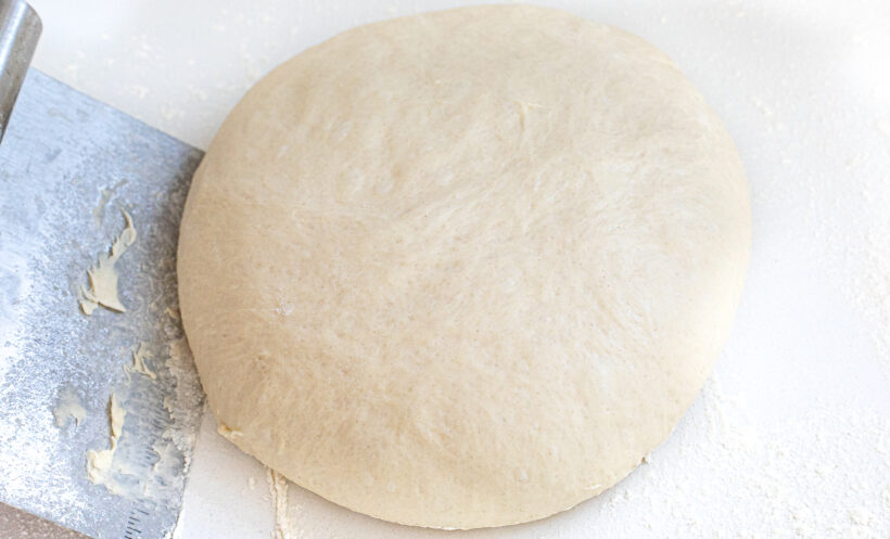Kneaded pizza dough on a floured countertop.