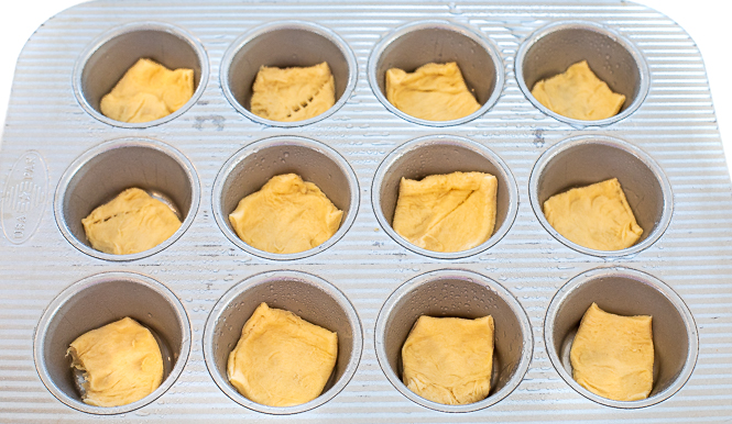 Crescent roll dough squares in a muffin tin. 