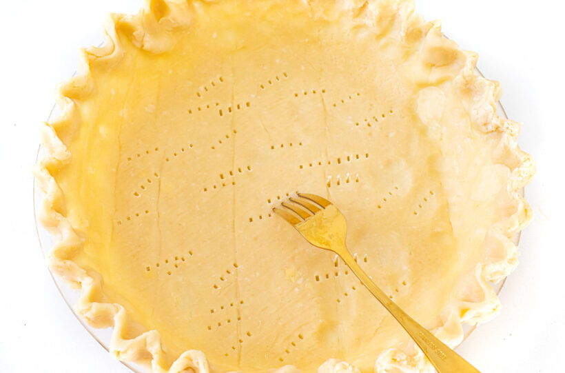 A gold fork poking holes into the pie crust.