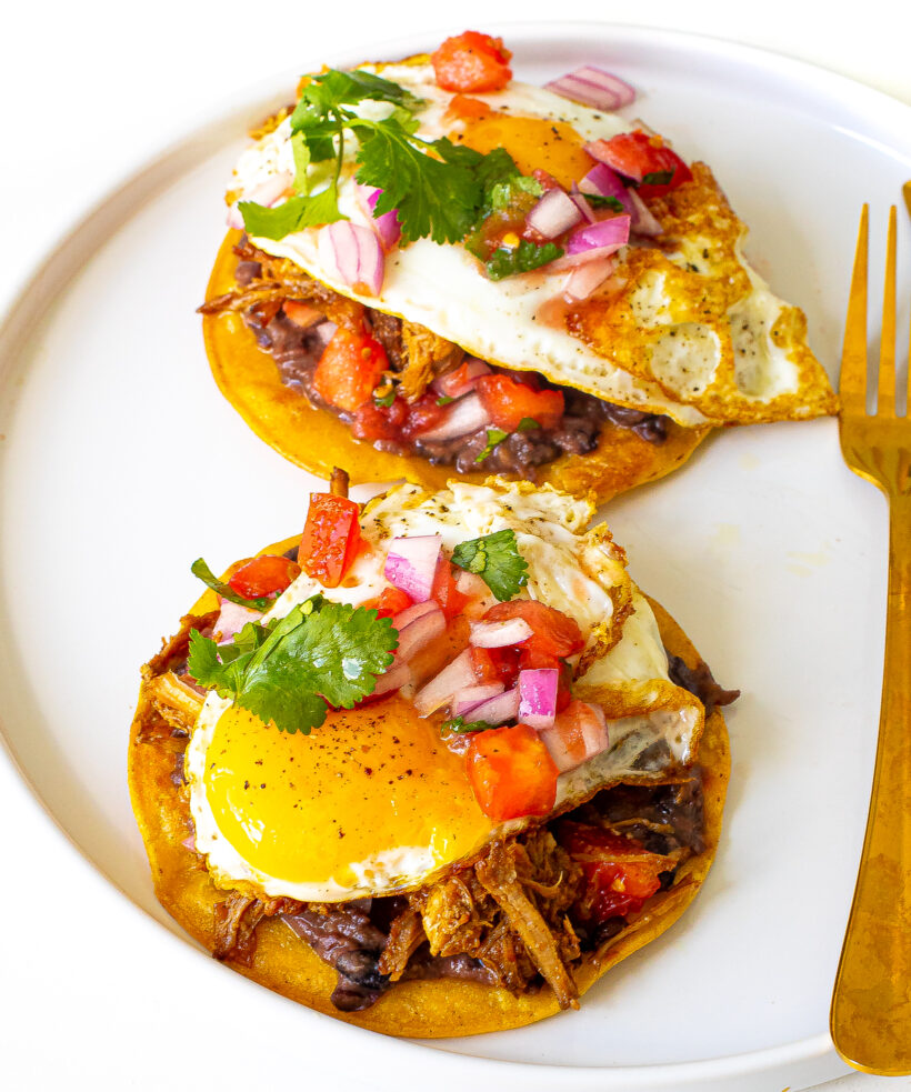 Pulled pork breakfast tostadas served on a plate with pico de gallo. 