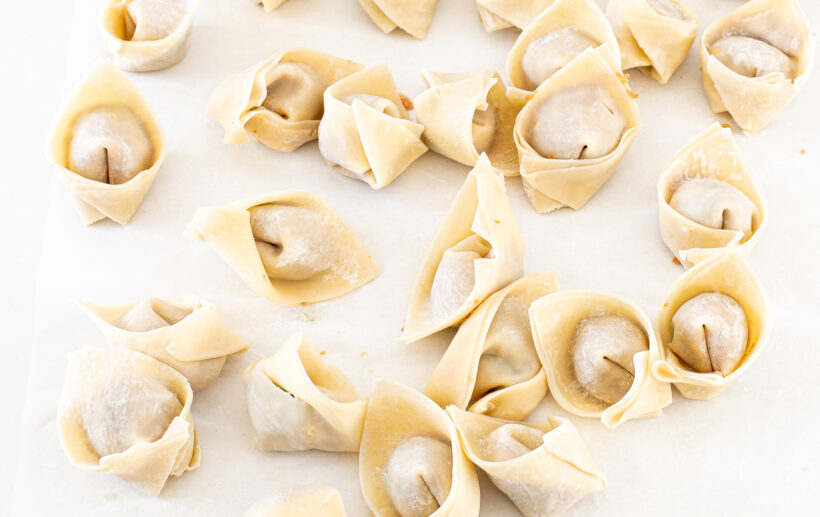 Uncooked folded wontons on a white surface.