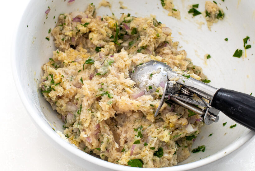 Greek chicken meatball mixture in a bowl with a cookie scoop.
