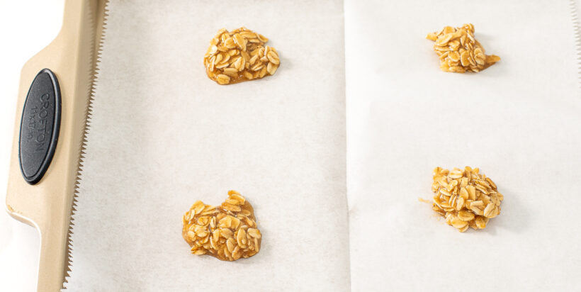 Cookie dough in heaps on a baking sheet lined with parchment paper. 