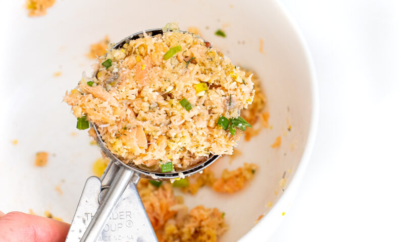 A cookie scoop scooping salmon cakes.