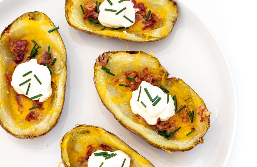 Air fryer potato skins with sour cream and green onions on top on a serving platter. 