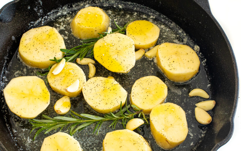 Melting potatoes starting to cook in a cast iron skillet with garlic and fresh rosemary. 