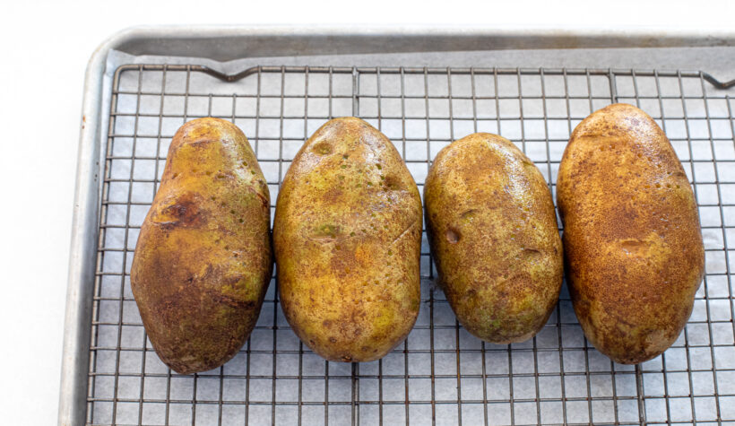 Four potatoes on a baking sheet lined with a wire rack. 