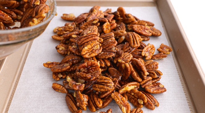 spreading candied maple pecans on a baking sheet lined with parchment paper