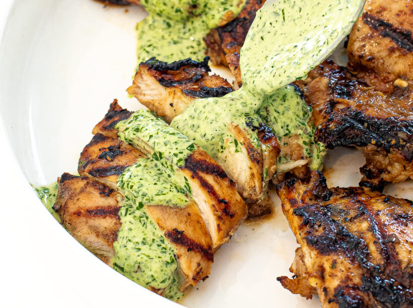 Green sauce being drizzled on top of grilled chicken. 