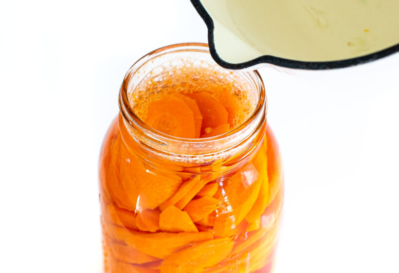 pouring brining liquid on top of sliced carrots in mason jar