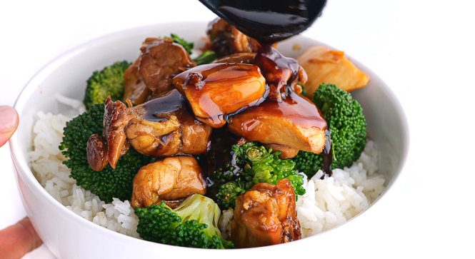 pouring sauce on top of chicken, broccoli and rice in white bowl