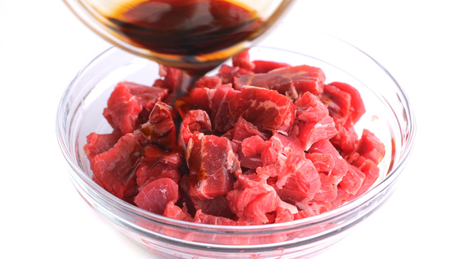 pouring soy sauce on top of flank steak in clear bowl