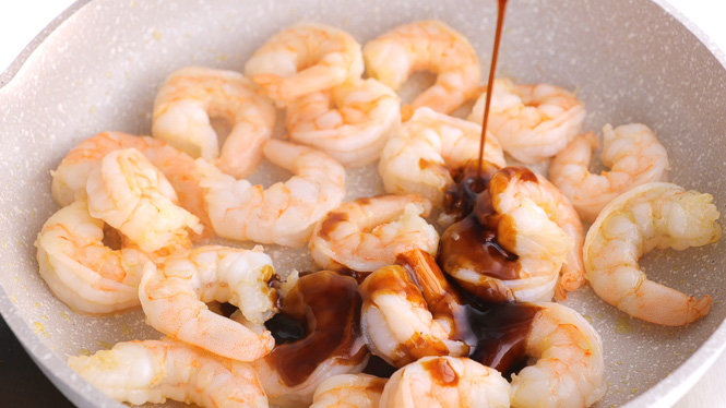 pouring teriyaki sauce on top of cooked shrimp.