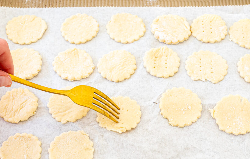 A hand holding a a fork, pricking holes into the crackers.