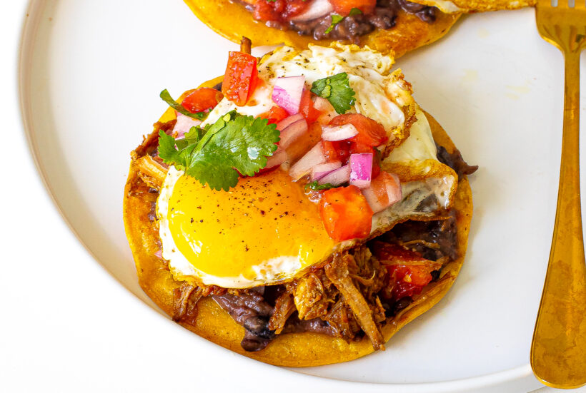 Breakfast tostada after being assembled and served on a white plate. 