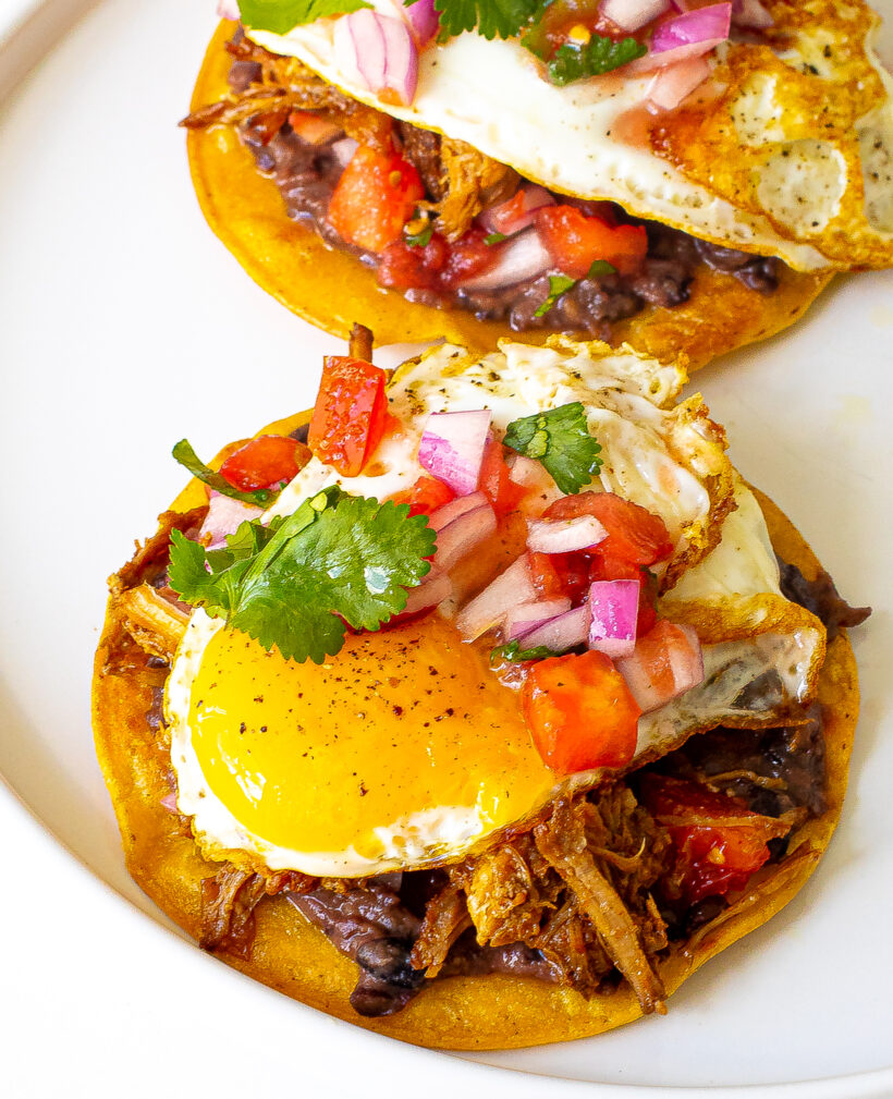Two pulled pork breakfast tostadas served on a white plate. 