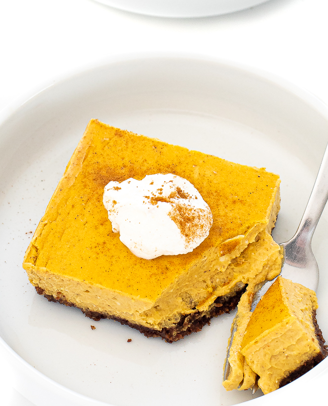 bite of pumpkin cheesecake bar on a white plate topped with whipped cream for thanksgiving menu