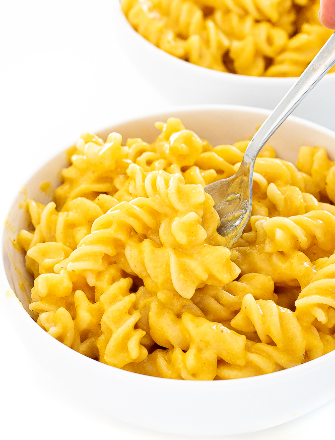 Mac and cheese in a white bowl being scooped by a silver spoon.