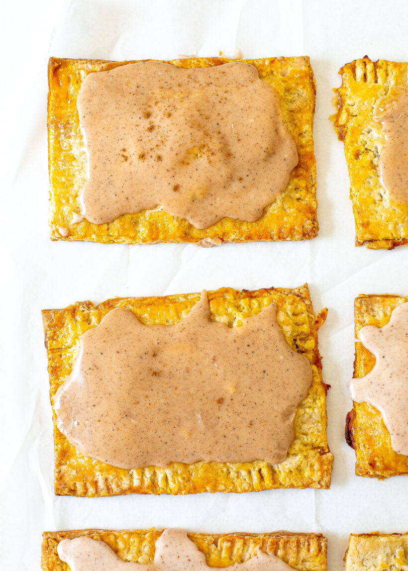 Freshly baked pop tarts with pumpkin spice glaze on a baking sheet.