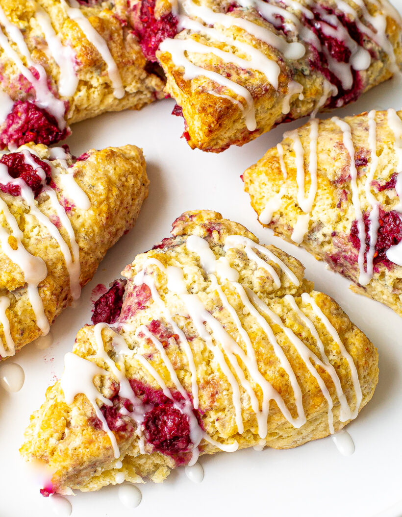 Raspberry scones drizzled with almond glaze and placed on a white plate.