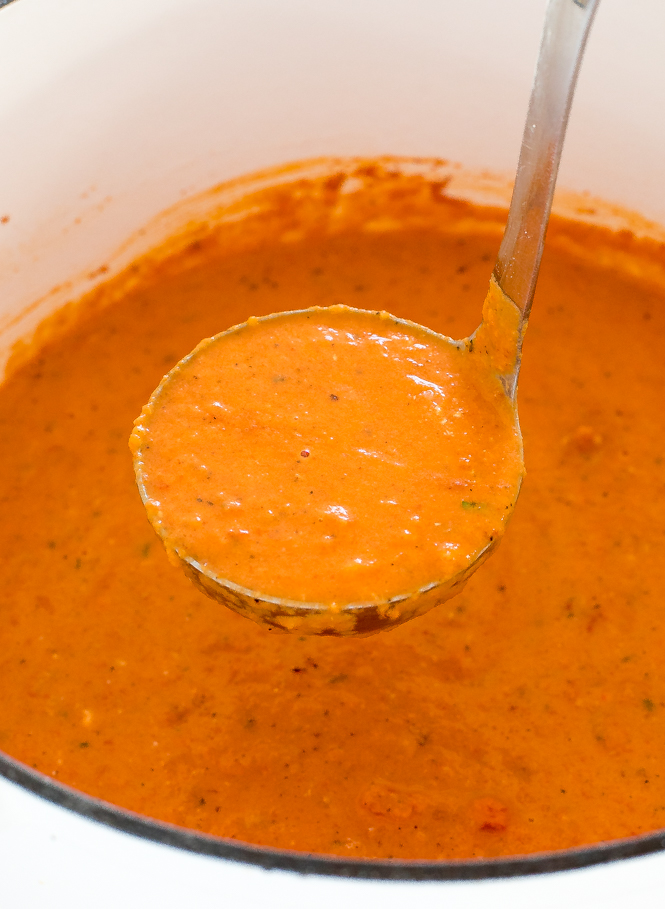 a closeup of this Creamy Roasted Red Pepper and Tomato Soup in a Dutch oven with a portion scooped out in a ladle